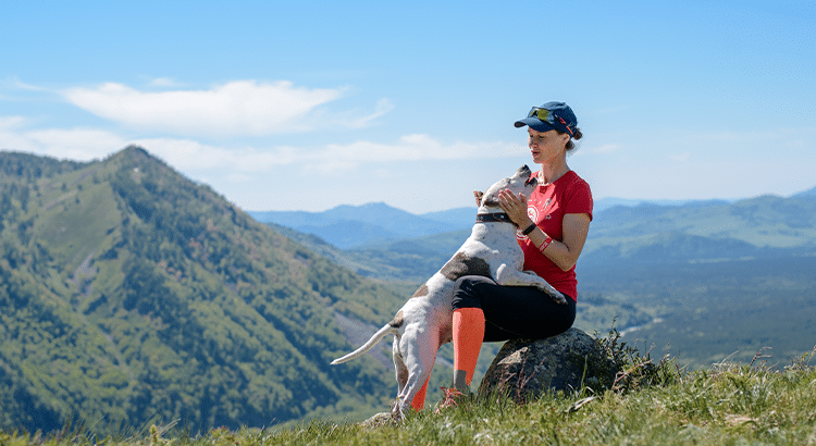 Athletic woman and a dog bonding on top of a mountain